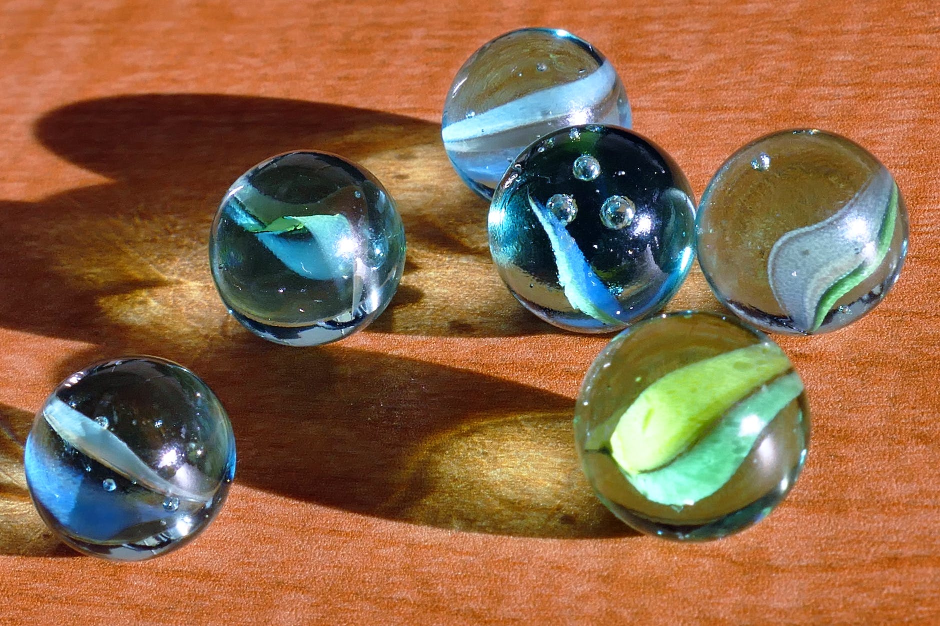 six blue and green marbles on brown surface